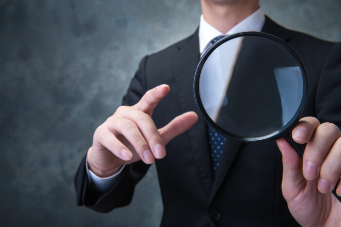 虫眼鏡を指すスーツ男性